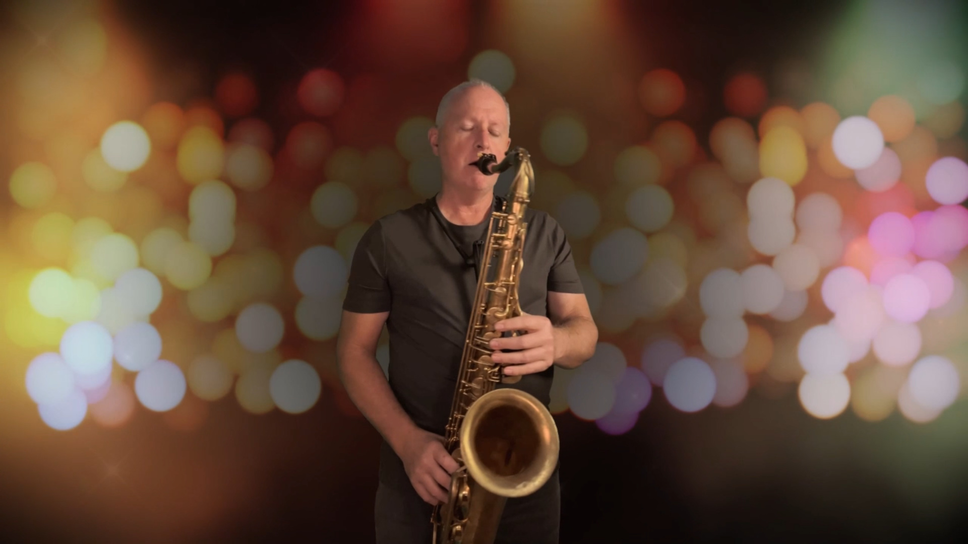 Andy playing tenor saxophone against a warm, colourful bokeh background.