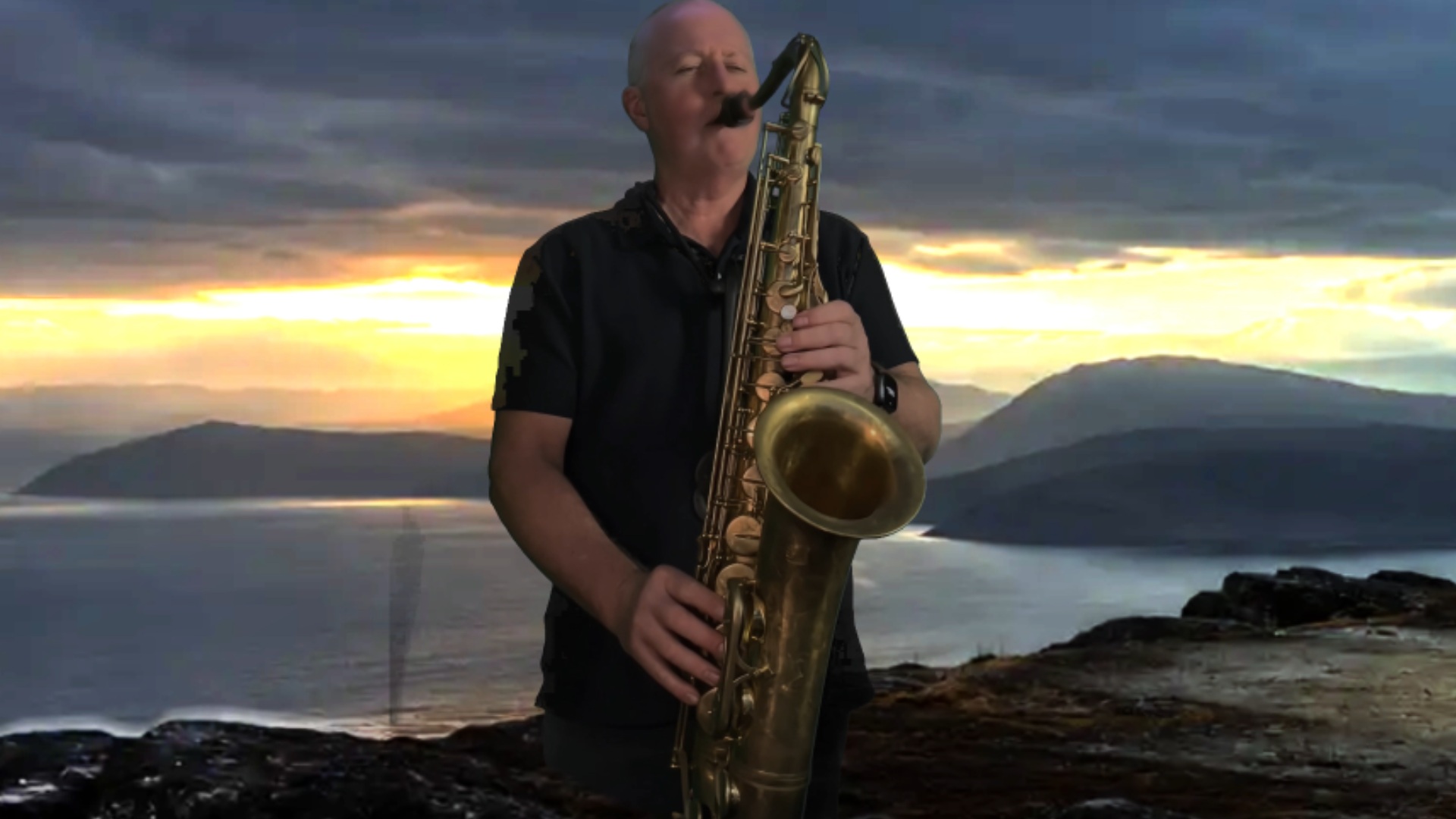 Andy Hungerford playing tenor saxophone against a dramatic coastal sunset backdrop.